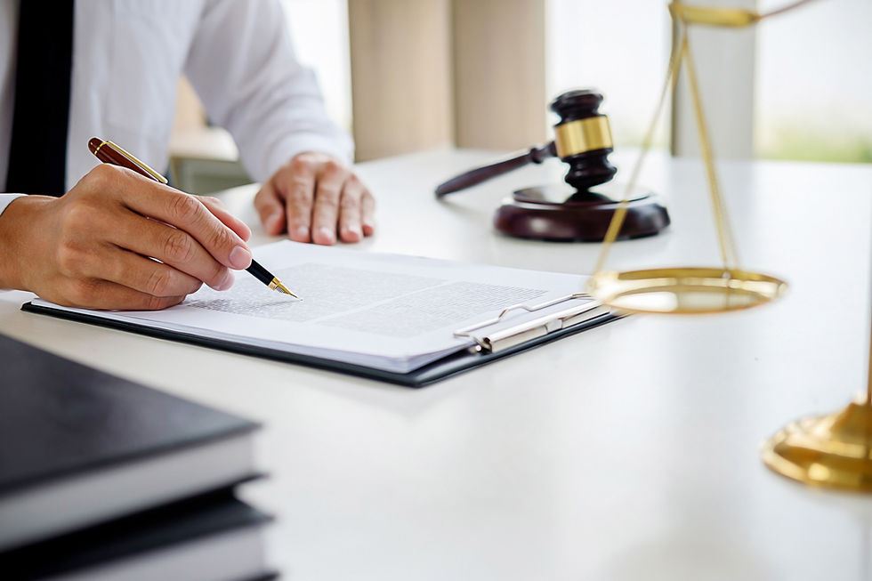 A man holding a pen, reviewing documents, gavel on the side with legal scales
