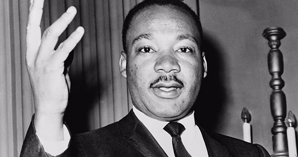 A black and white image of Dr. Martin Luther King Jr. raising his hand and speaking.
